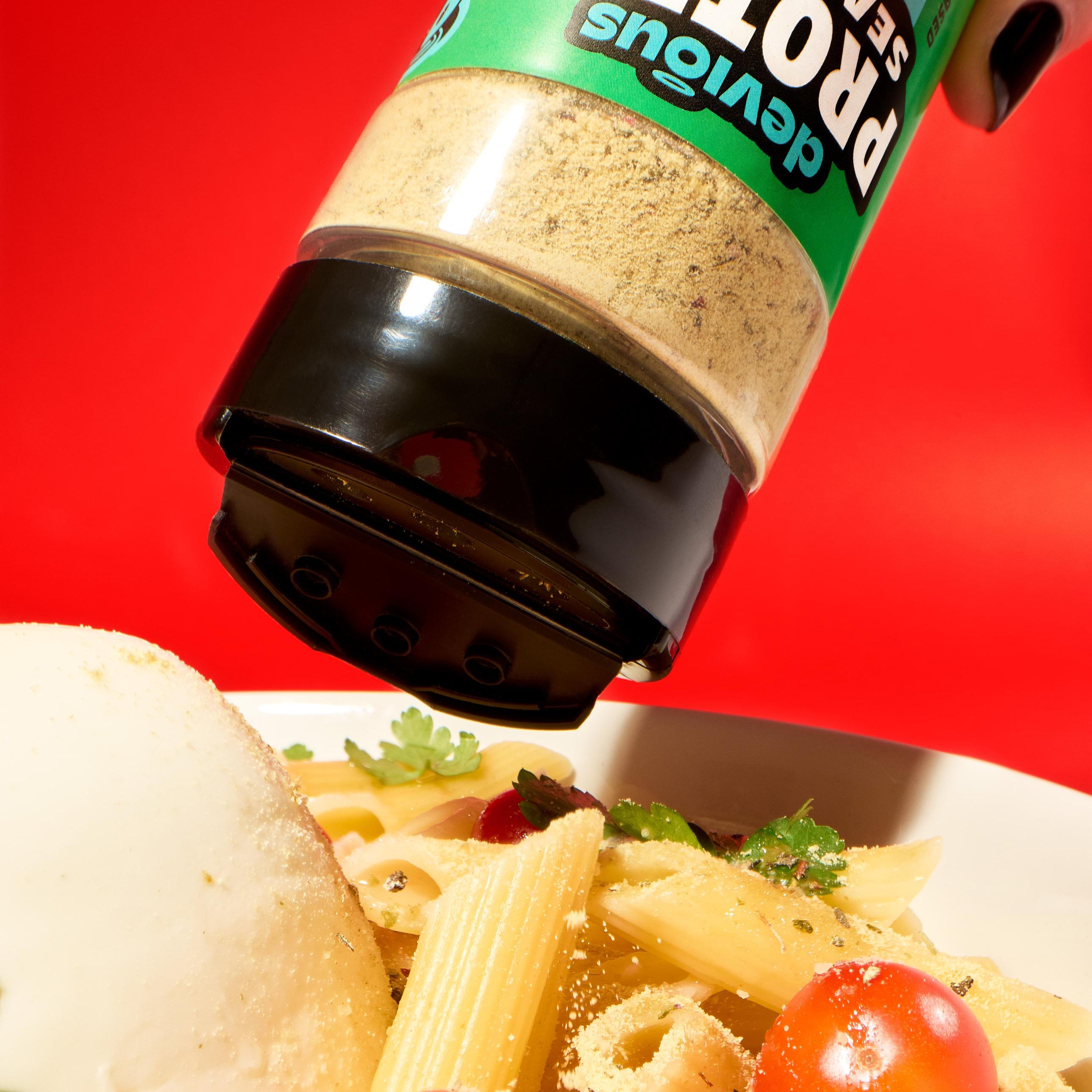 Pasta dish with protein seasoning being sprinkled on it against a red background
