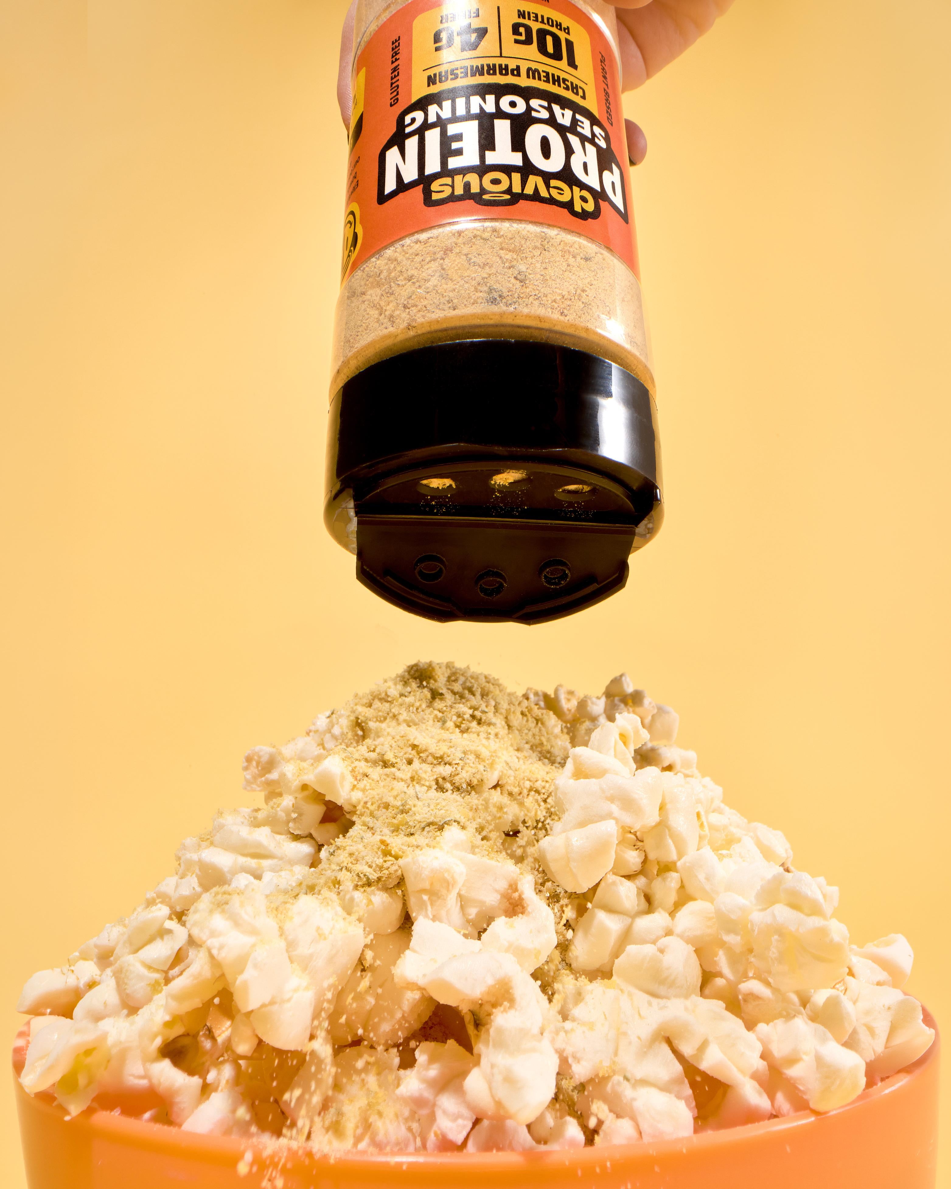 Protein powder being sprinkled onto popcorn with a yellow background