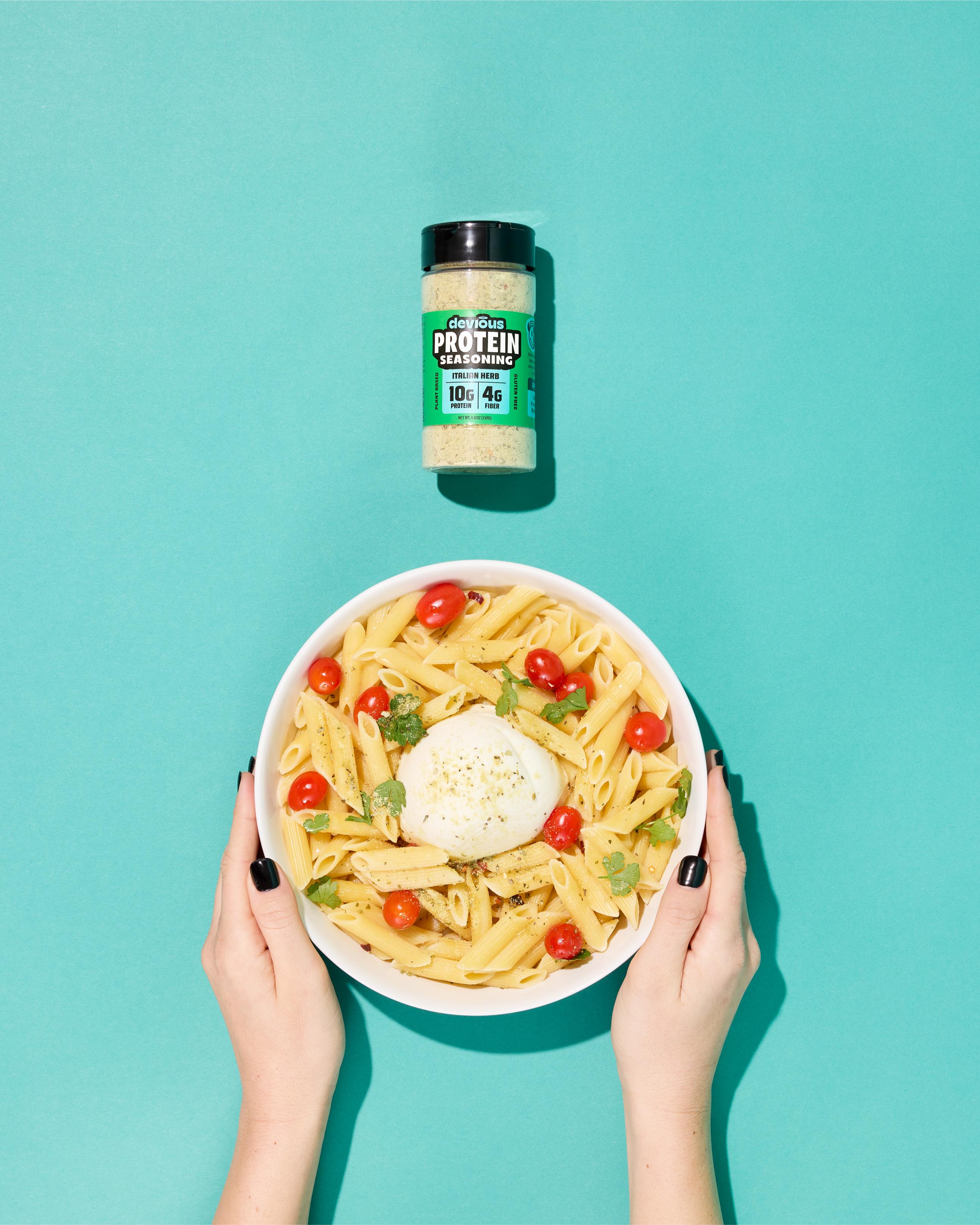 Bowl of pasta with a protein supplement jar on a teal background