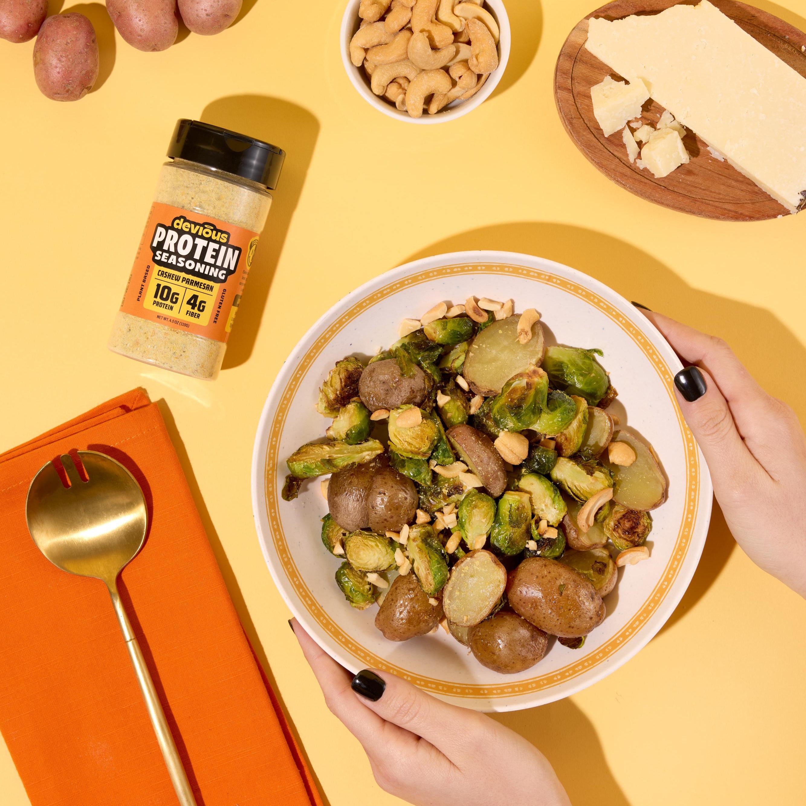 Person holding a bowl of roasted vegetables with a container of protein powder on a yellow background