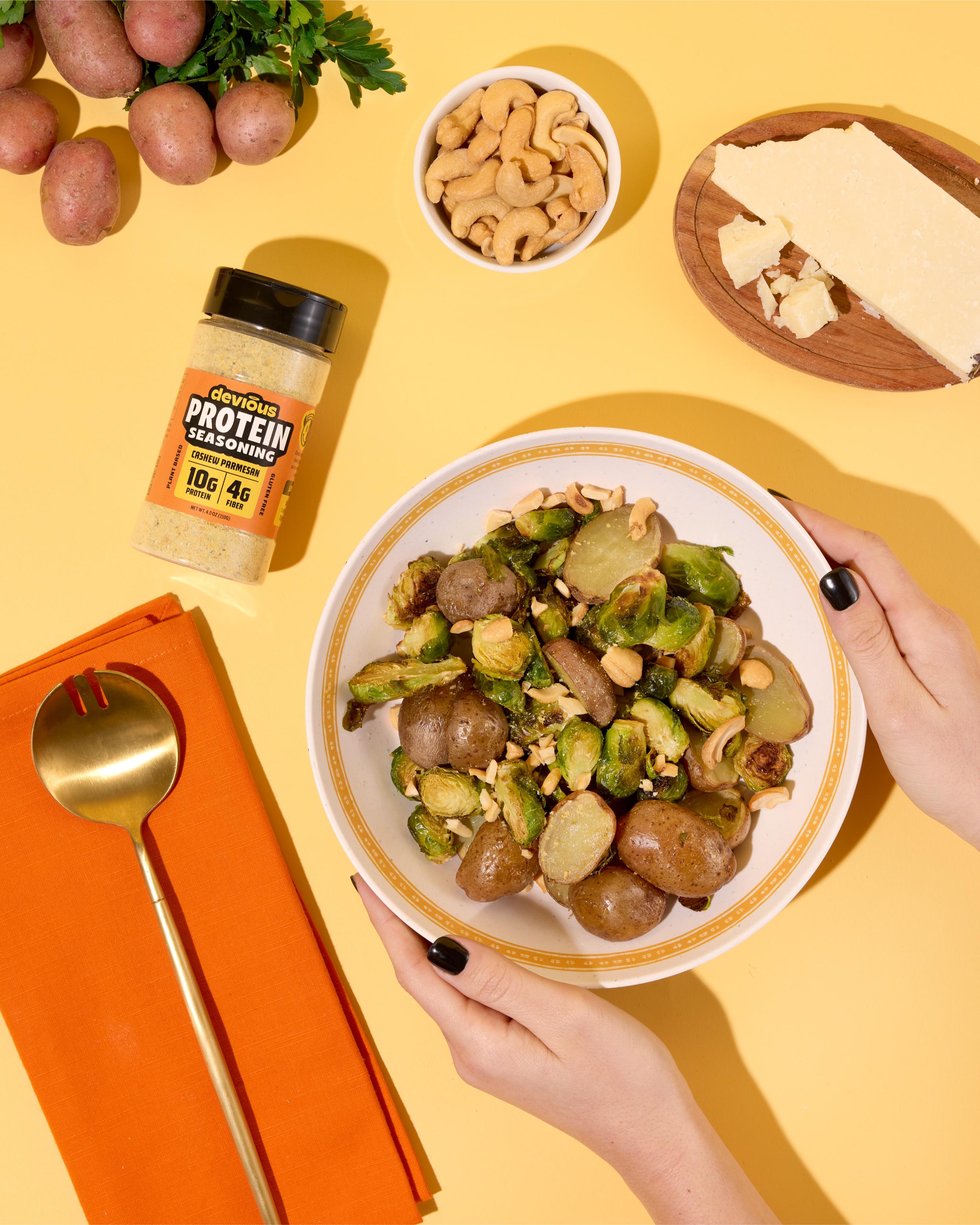 Person holding a bowl of roasted vegetables with a container of protein powder on a yellow background